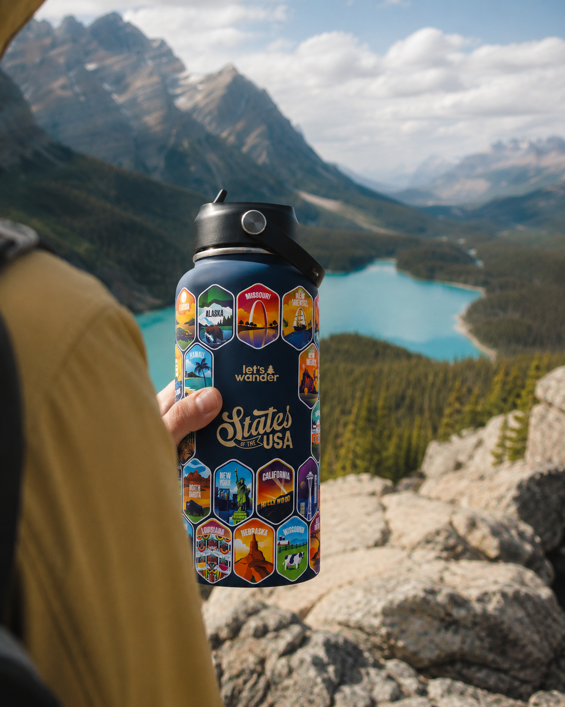 Let’s Wander States of the USA water bottle held by a hiker overlooking a mountain lake.